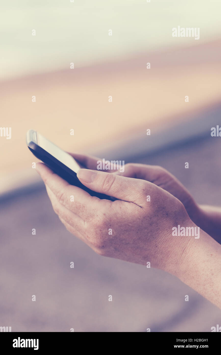 Retrò tonica femmina adulta mani usando il telefono cellulare all'aperto, l'uso di tutti i giorni del dispositivo elettronico per la comunicazione Foto Stock