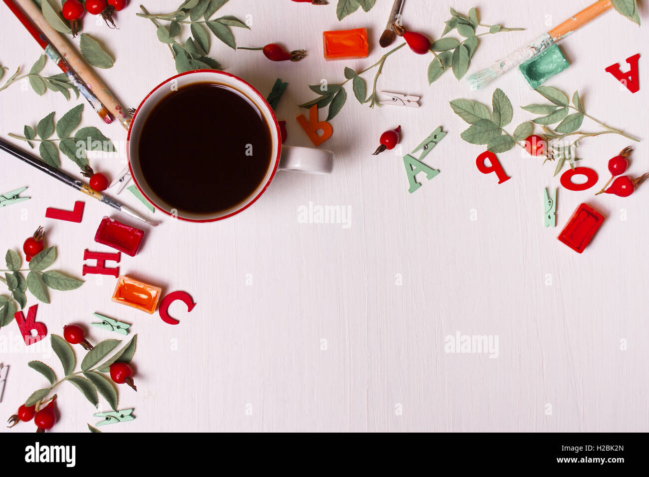 Vista superiore del designer desktop con tazza di caffè, fiori, matita ,spazzole, vernice, foglie, bria, lettere Foto Stock