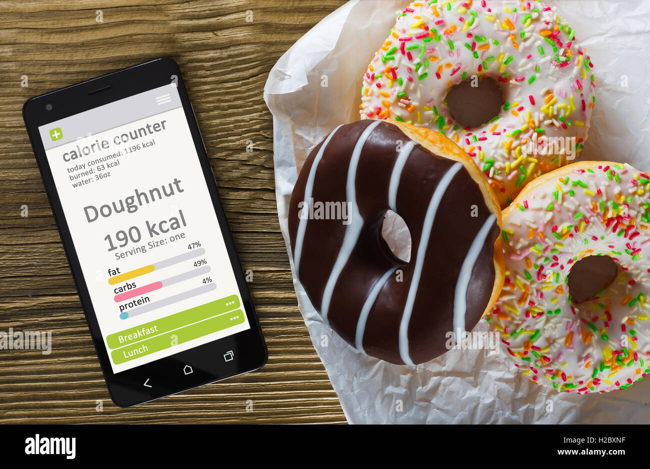 Calorie Counter concetto - telefono cellulare con contatore di caloria app sullo schermo e ciambelle. Tavolo in legno come sfondo Foto Stock