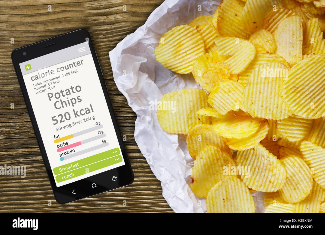 Calorie Counter concetto concetto - telefono cellulare con contatore di caloria app sullo schermo e patatine. Tavolo in legno come backgrou Foto Stock