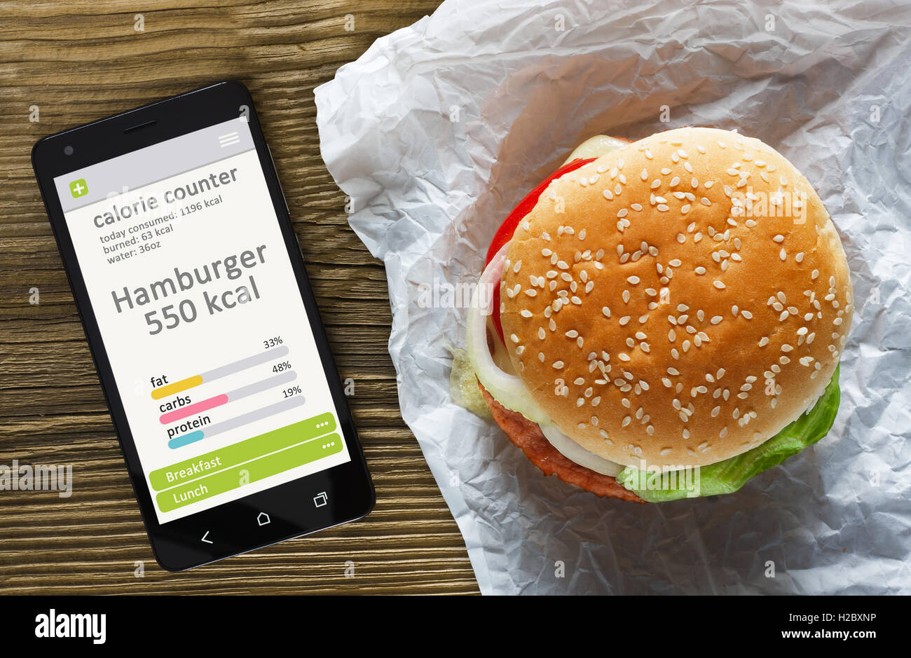 Calorie Counter concetto - telefono cellulare con contatore di caloria app sullo schermo e hamburger. Tavolo in legno come sfondo Foto Stock