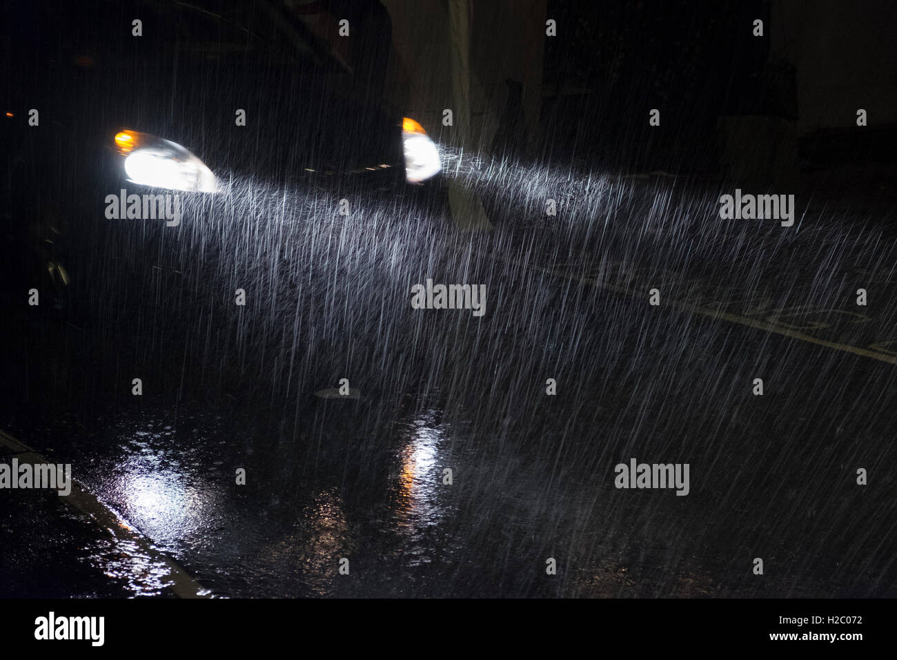 Un auto fari Shine attraverso pesanti piogge durante la notte Foto Stock