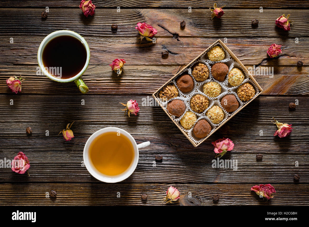 Sweet Food pattern. Scatola di tartufi di cioccolato, i chicchi di caffè, secco rose fiori, una tazza di caffè nero e tè verde sul tavolo di legno Foto Stock