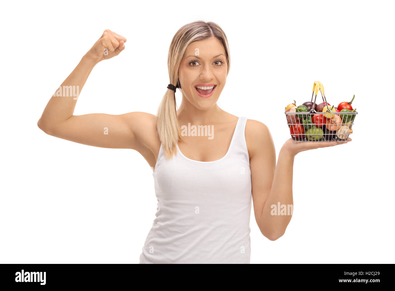 Donna sorridente tenendo un piccolo carrello pieno di frutta e verdura e flettendo il suo bicipite isolato su sfondo bianco Foto Stock