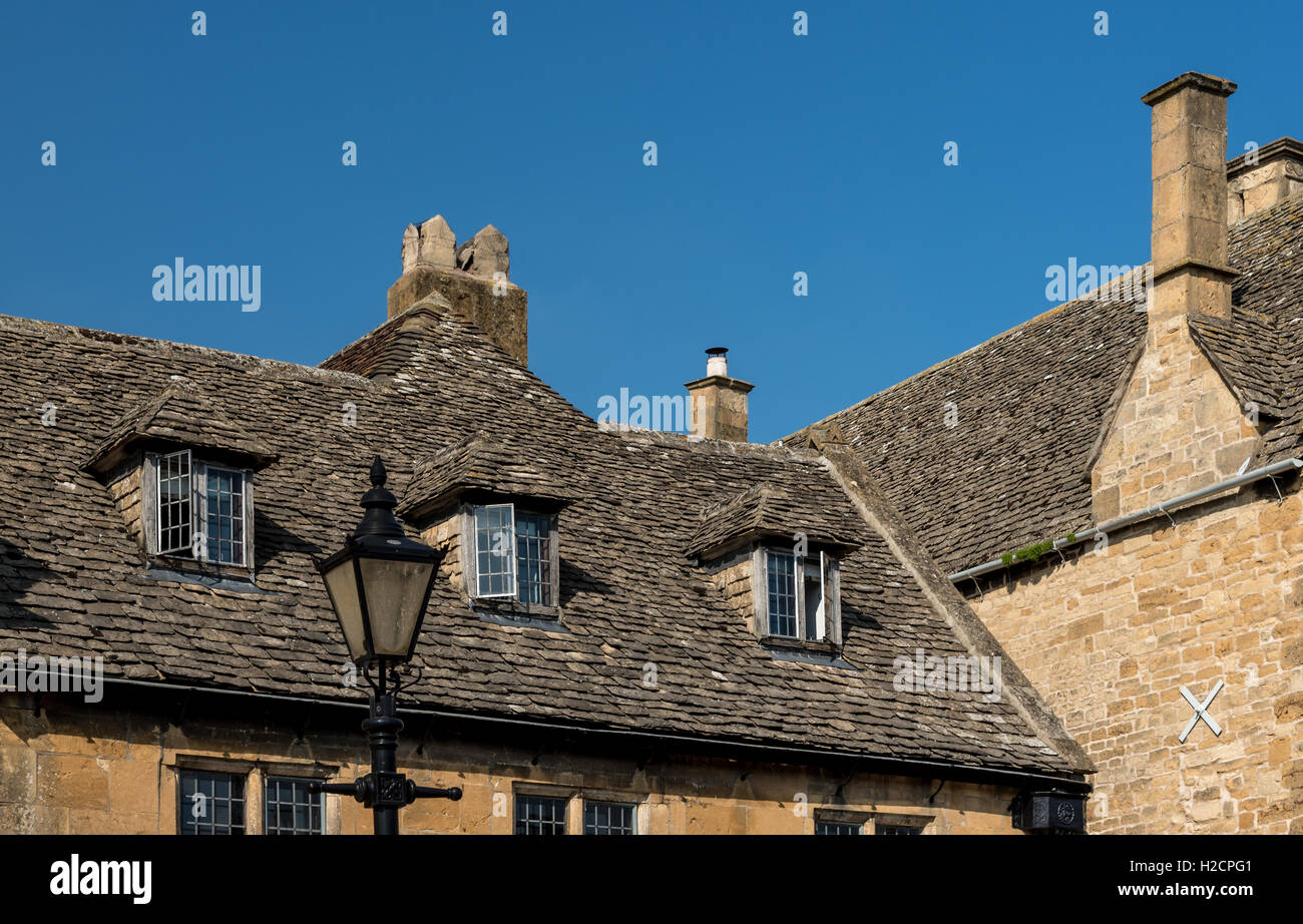 Vecchio Cotswold stone tetto di tegole con finestre dormer, camini e la vecchia strada lampada Foto Stock