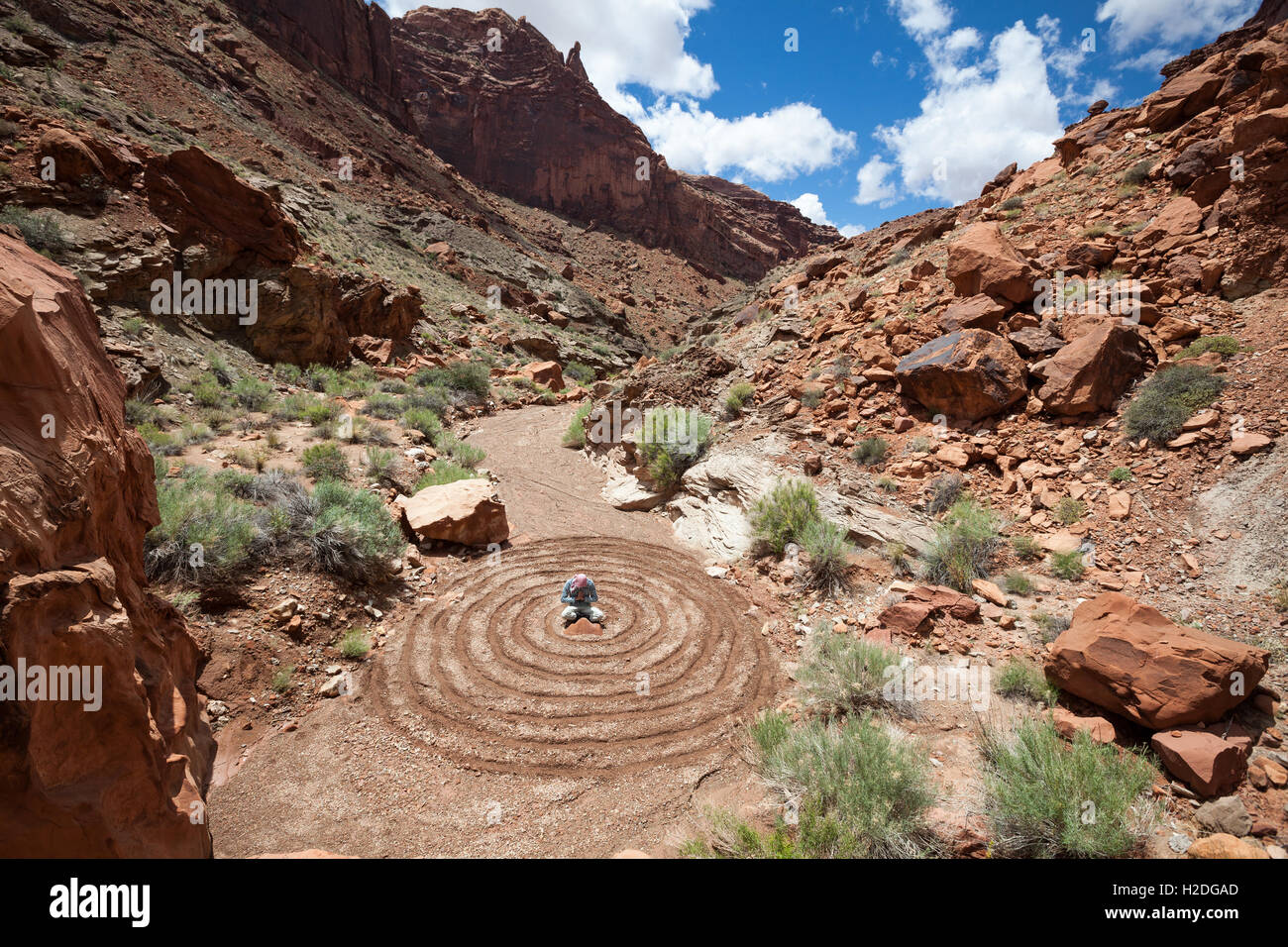 Un uomo meditando o pregando il centro di un disegno a spirale nel deserto Foto Stock