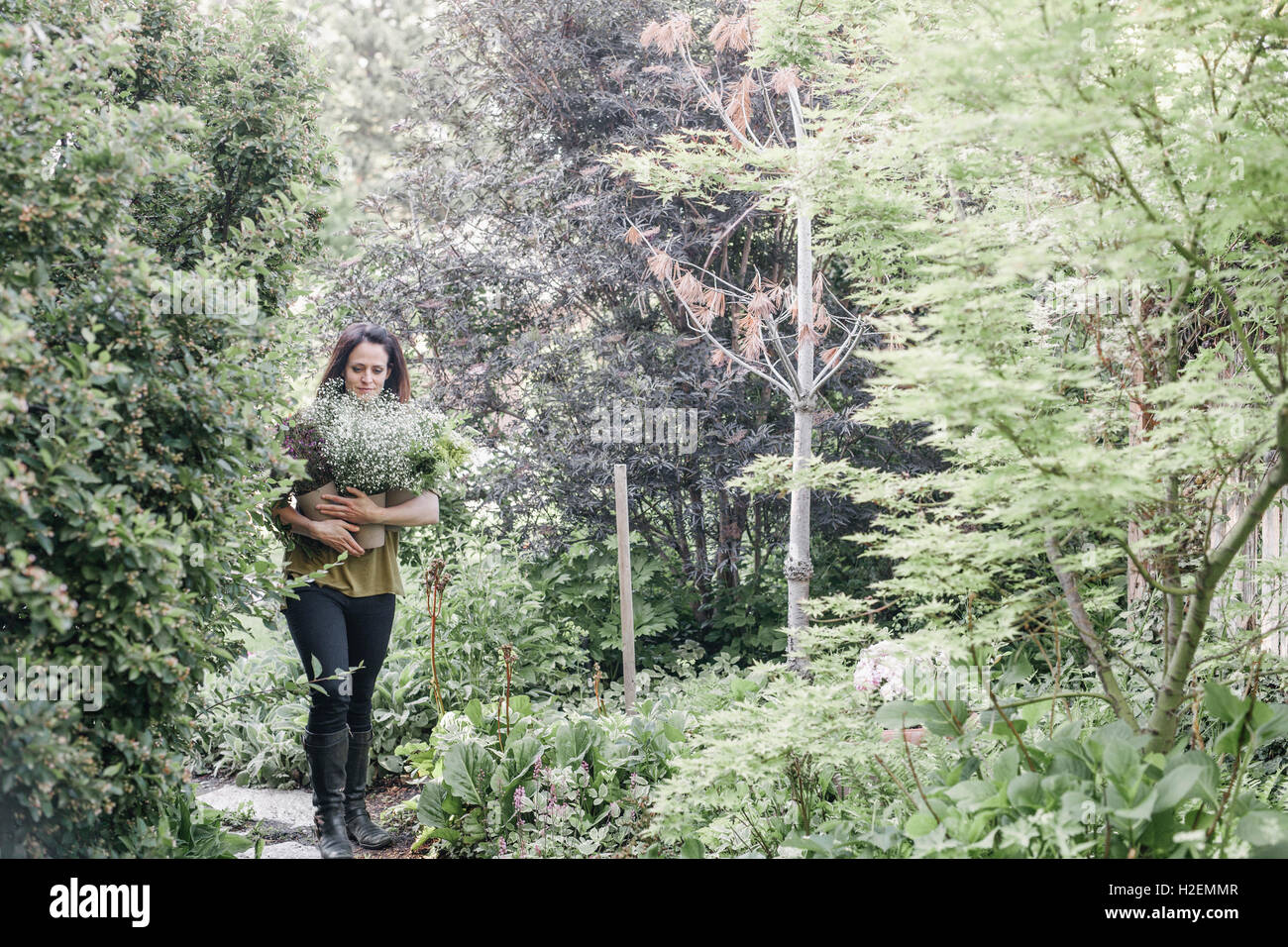 La donna a piedi attraverso un giardino, portando un grosso mazzo di fiori. Foto Stock