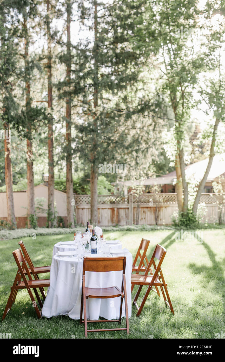 Impostare il tavolo con una tovaglia bianca e sedie di legno in un giardino. Foto Stock