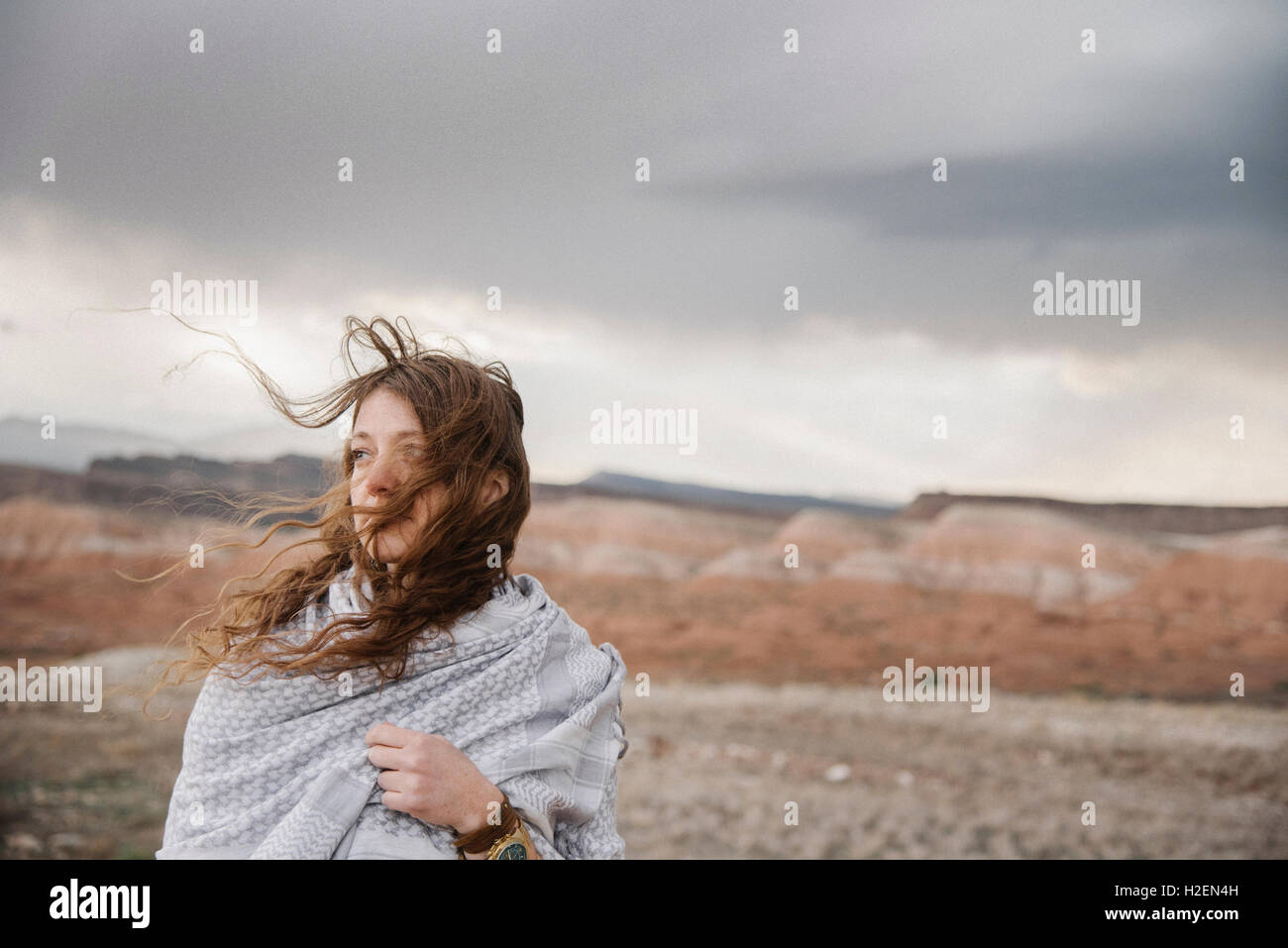 Una donna con lon g capelli al vento in piedi in un paesaggio desertico. Foto Stock
