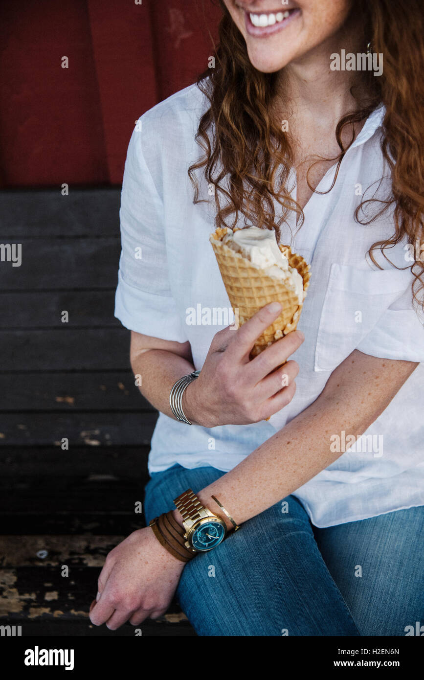 Donna con lon g marrone capelli seduta su una panchina a mangiare il gelato. Foto Stock
