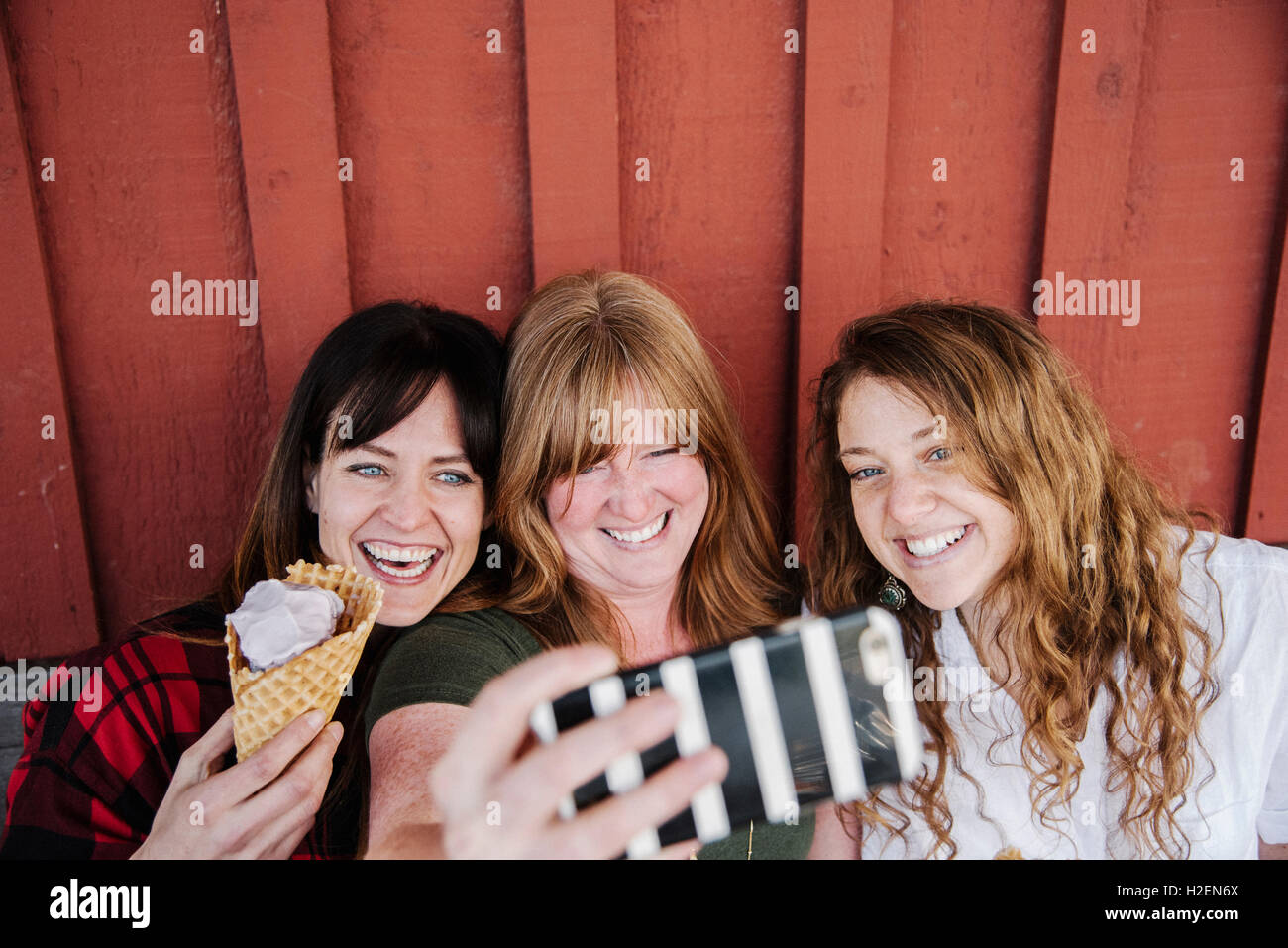 Tre donne mangiare il gelato, prendendo un selfie con un telefono cellulare. Foto Stock