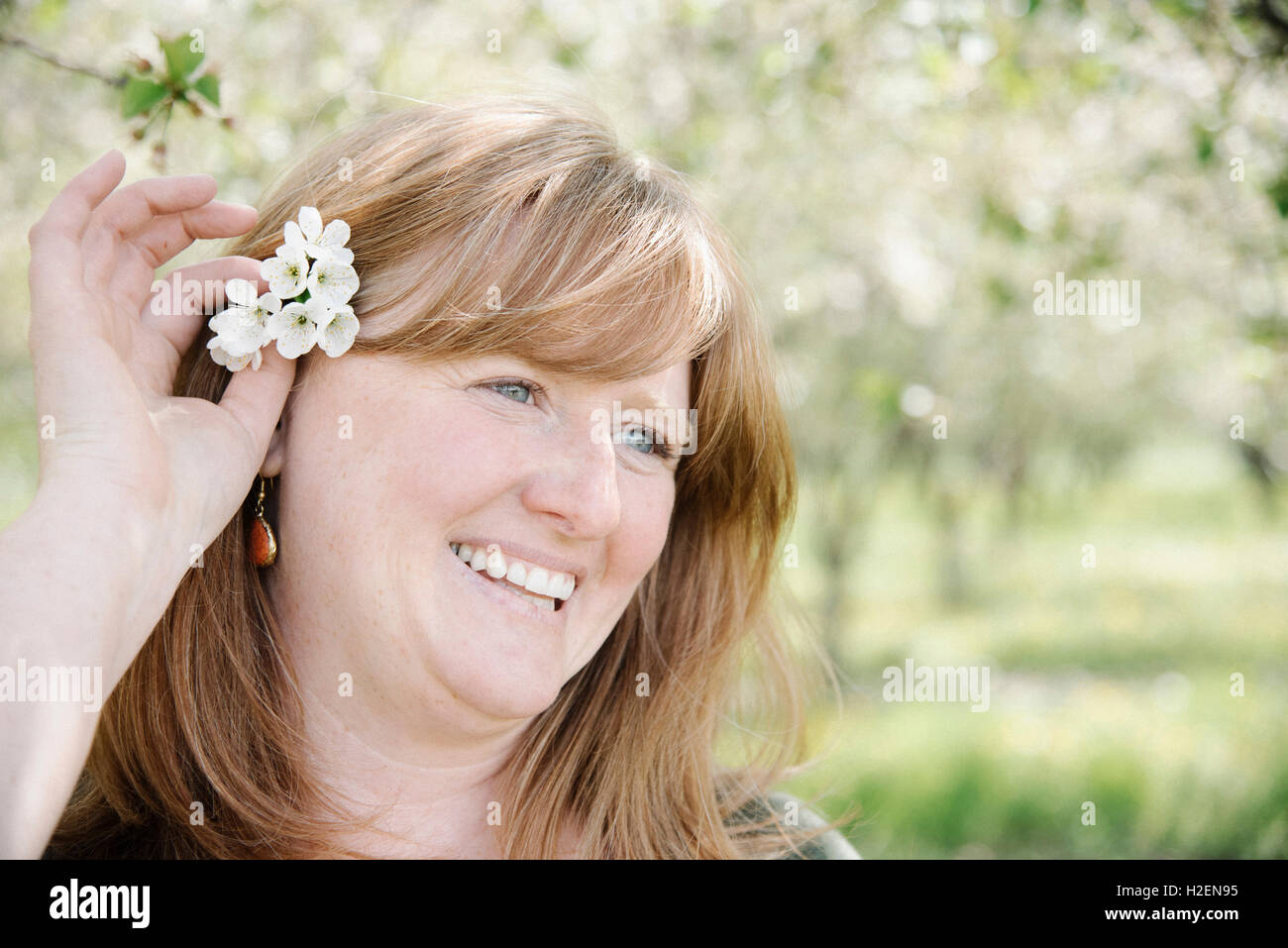 Donna che mantiene un fiore nella sua capelli rossi, ridendo. Foto Stock