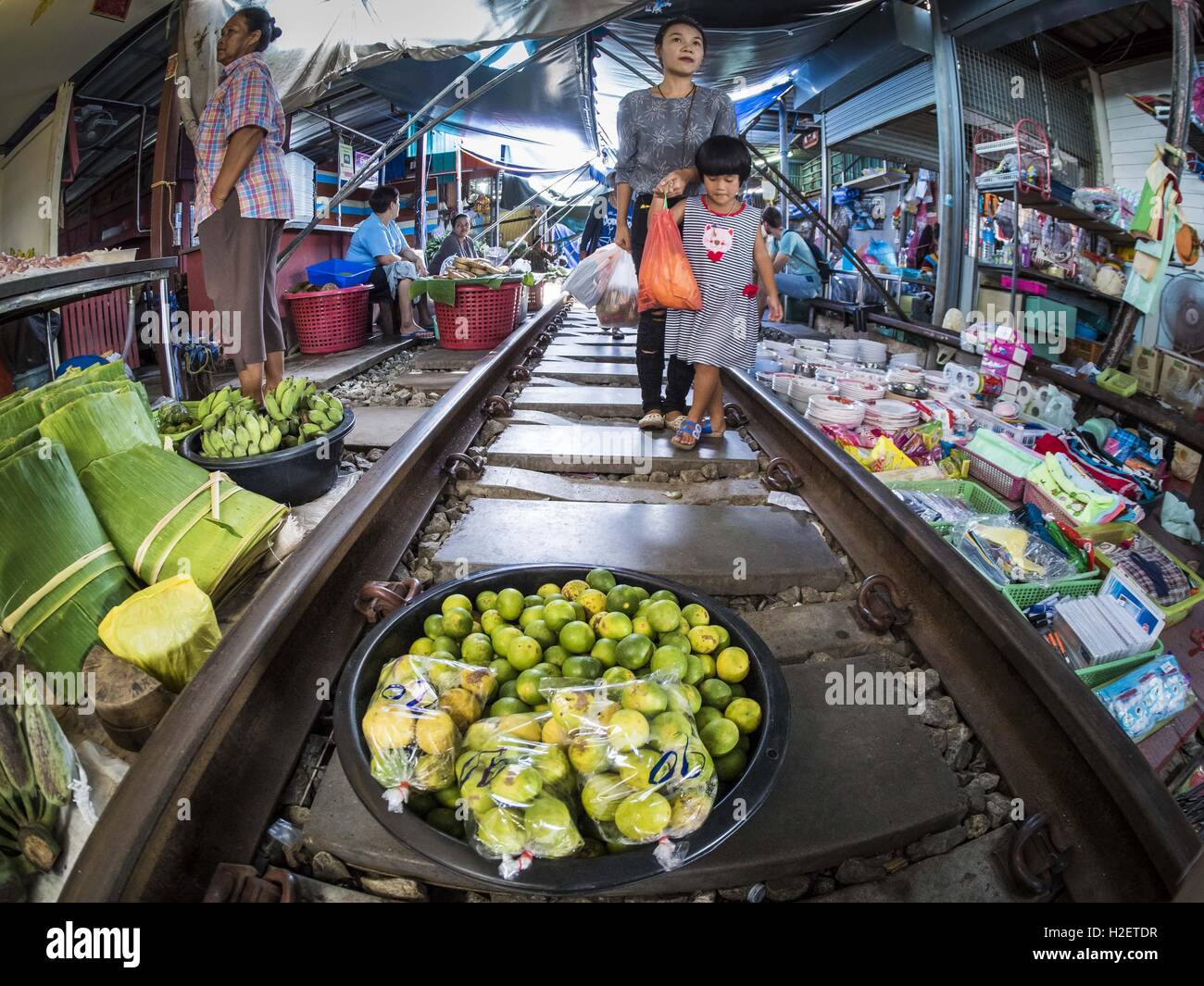 Samut Songkhram, Samut Songkhram, Thailandia. Il 27 settembre, 2016. Una madre e figlia a piedi lungo le piste, passato un stand con vendita di limes nel mercato della stazione ferroviaria in Samut Songkhram. Il treno da Baen Laem a Samut Songkhram (Mae Khlong) ha recentemente ripreso servizio. Il 33 chilometro via era chiusa per la riparazione per quasi un anno. In Samut Songkhram, il treno passa sul mercato. I fornitori a tirare le loro spicca il modo e le persone passo al di fuori della modalità appena il treno passa attraverso il mercato. È una delle più famose stazioni ferroviarie in Tailandia ed è diventato un importante ufficio del turism Foto Stock