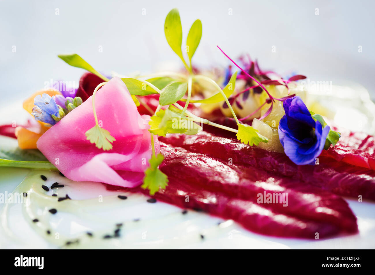 Carpaccio e guarnite di pisello freschi germogli e fiori commestibili su una piastra bianca. Foto Stock