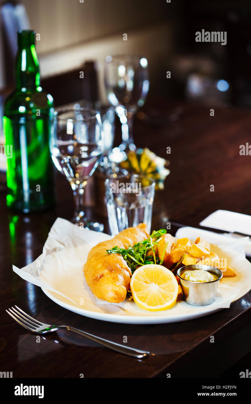 Borgo Casa pubblica il cibo. Una cotta corso principale, piatto su un tavolo da pranzo, pesce e patatine. Bicchiere di acqua e una bottiglia di colore verde. Foto Stock