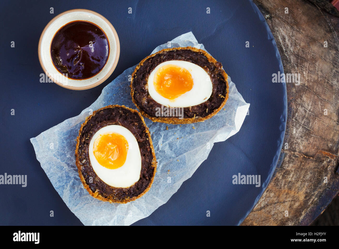 Village pub cibo. Un piatto di blu con una fresca fatta scotch egg tagliati in due e una pentola di salsa. Foto Stock