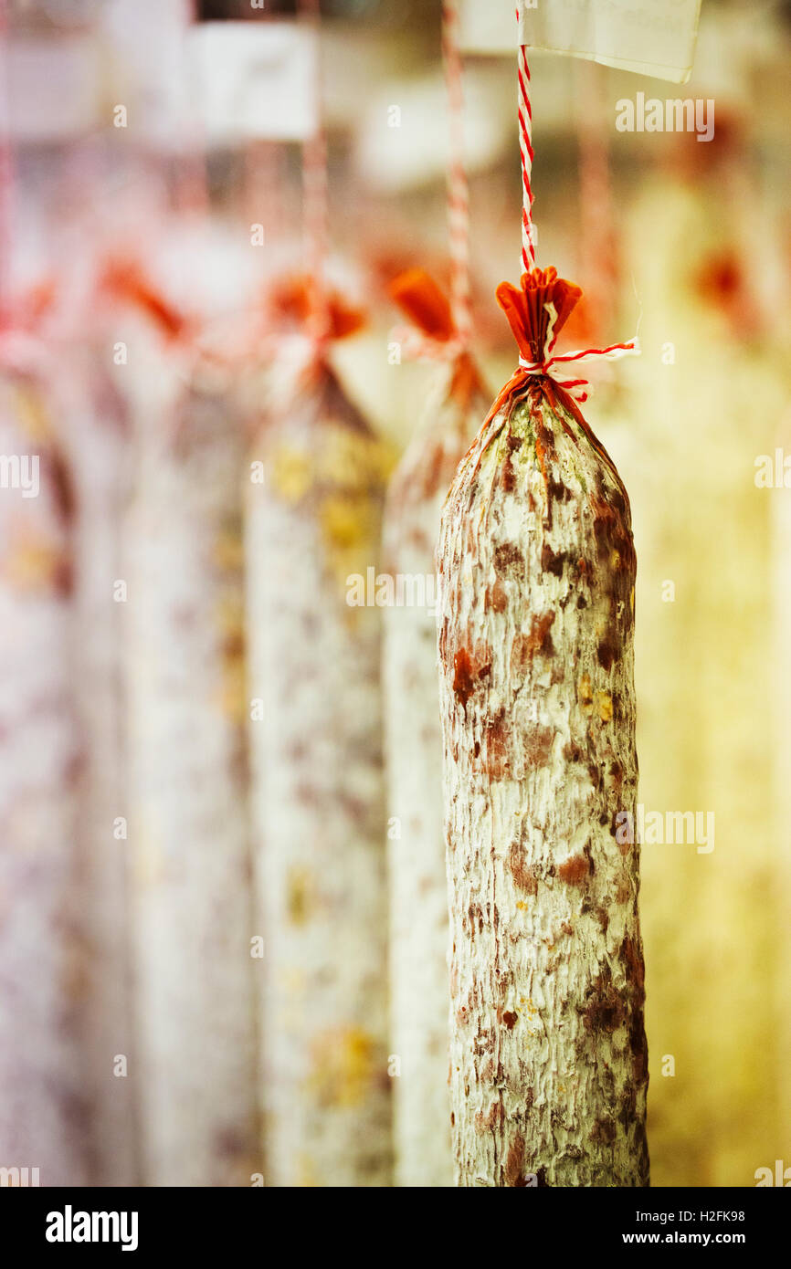 Close up di carne di maiale e aglio salami appesi da ganci in una charcuterie. Foto Stock