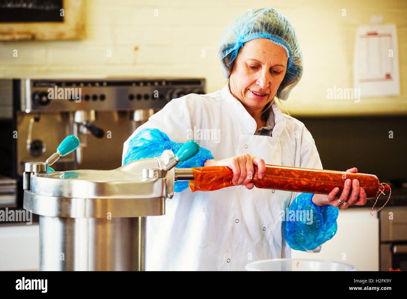 La donna lavora in una macelleria, indossare indumenti protettivi e guanti, il riempimento di un involucro con il salame chorizo carne. Foto Stock