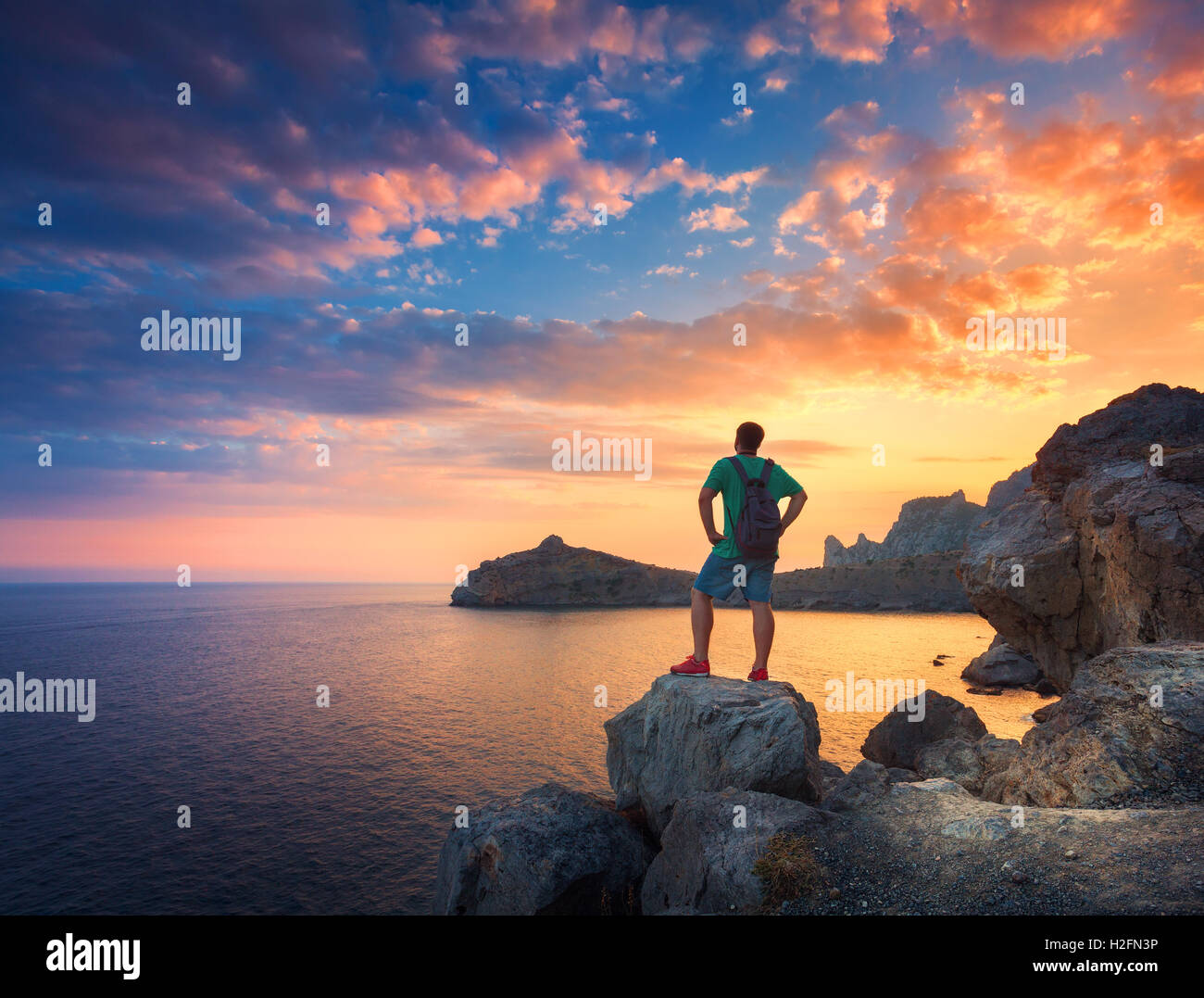 Bella estate paesaggio con uomo in piedi con zaino sulla pietra all'oceano contro il cielo colorato con nuvole a Sun Foto Stock
