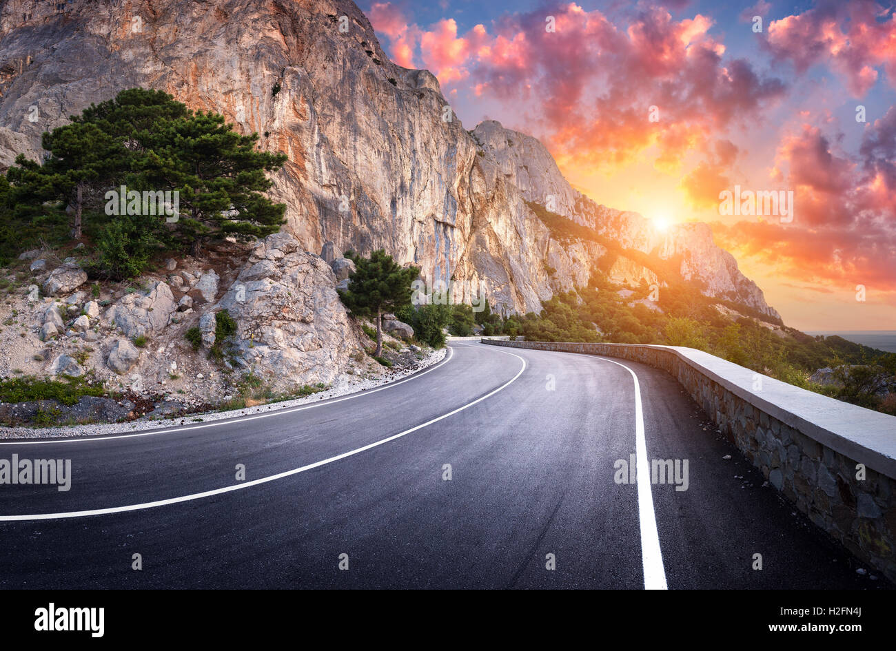 Strada asfaltata. Paesaggio con una bella strada di montagna con un asfalto perfetto in serata. Alte rocce, incredibile cielo a s Foto Stock