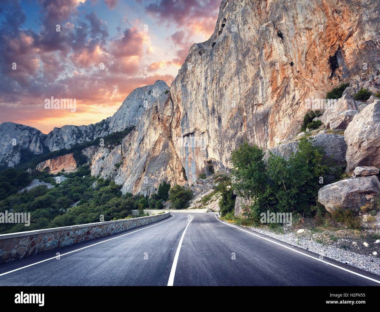 Bella strada asfaltata. Colorato paesaggio con alte rocce, strada di montagna con un asfalto perfetto, alberi e incredibile cielo nuvoloso una Foto Stock