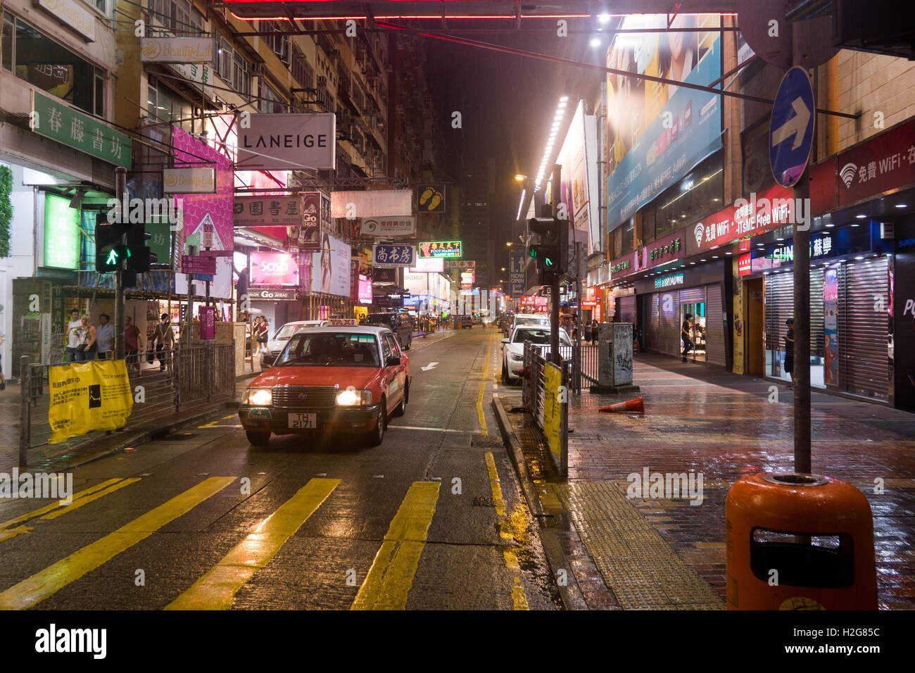 Un taxi attende al semaforo su una tranquilla notte piovosa a Hong Kong Foto Stock