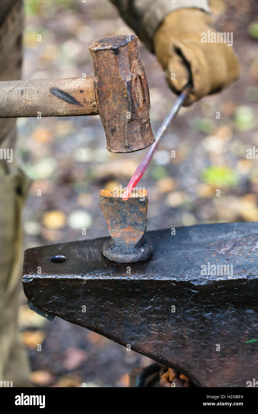 Fabbro costolette di asta di ferro con un martello e scalpello a incudine in outdoor fucina rurale Foto Stock