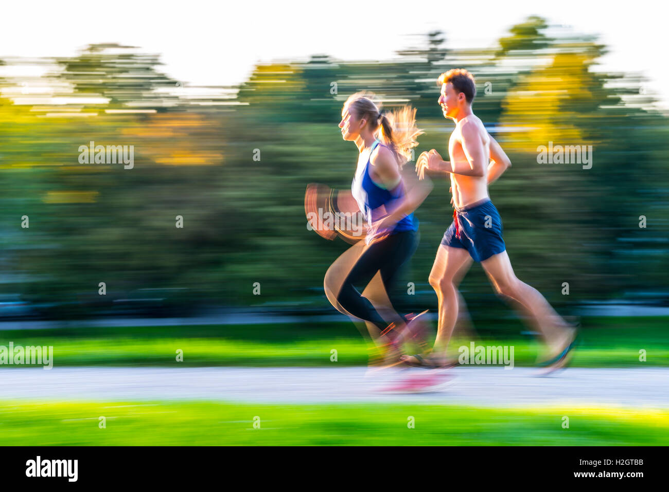 Il panning shot, giovane donna e giovane uomo in sportswear jogging attraverso il parco, Monaco di Baviera, Baviera, Baviera, Germania Foto Stock