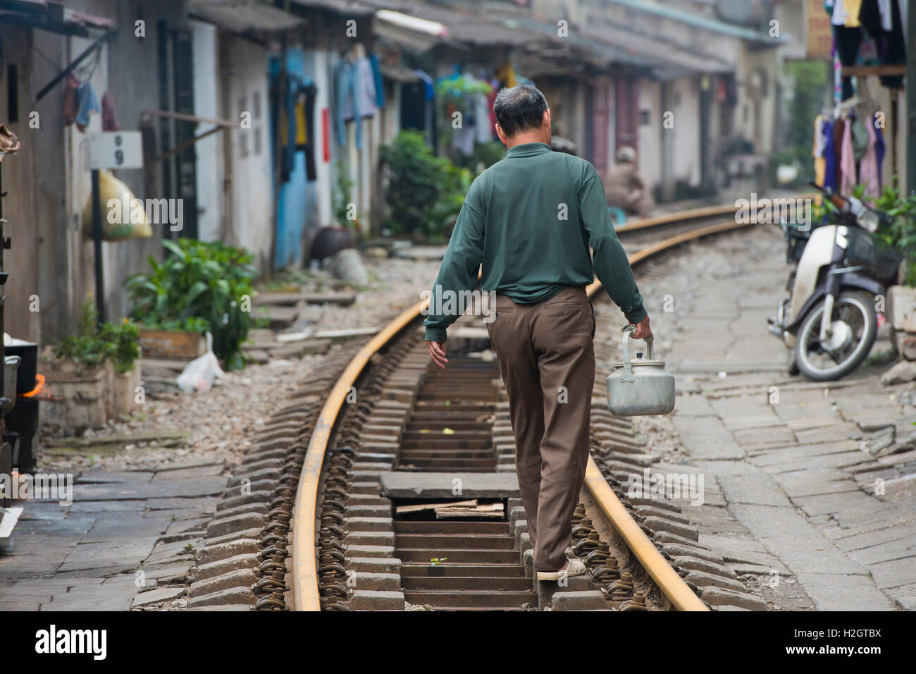 Uomo con bollitore camminando sul binario ferroviario, vivere accanto ai binari del treno, centro città, Hanoi, Vietnam Foto Stock