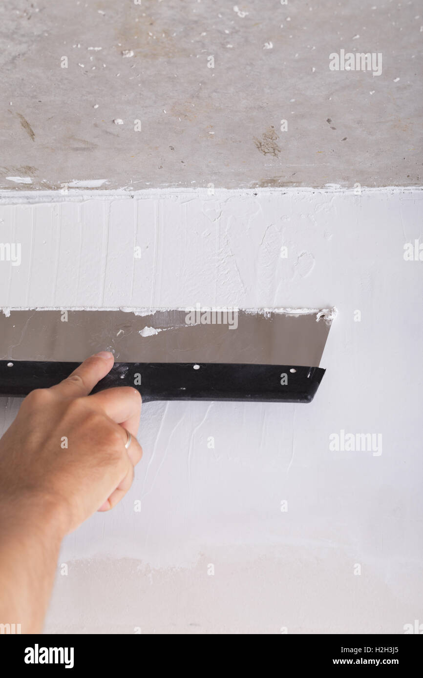 Miglioramento della casa da lavoratore mette lo strato di finitura di stucco sulla parete utilizzando una spatola di intonacatura Foto Stock