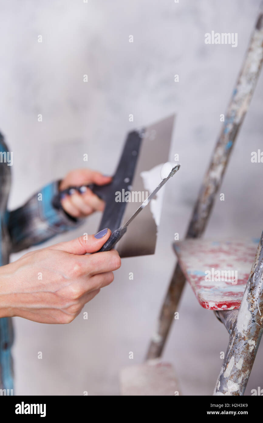 Miglioramento della casa da donna lavoratore mette lo strato di finitura di stucco sulla parete utilizzando una spatola di intonacatura Foto Stock