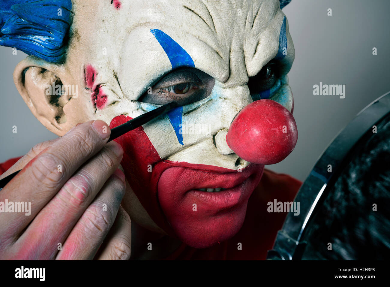 Primo piano di un giovane uomo che compongono se stesso come un male clown, utilizzando uno specchio Foto Stock