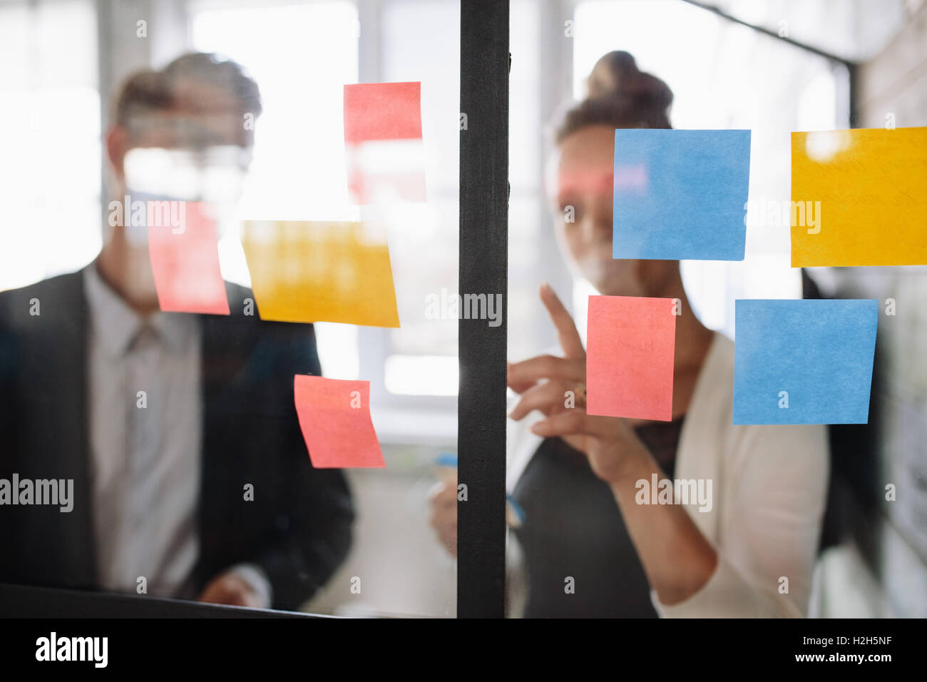 Due colleghi di lavoro lavorando sul progetto insieme. Business donna puntando alla nota adesiva al collega di sesso maschile sulla parete di vetro in o Foto Stock