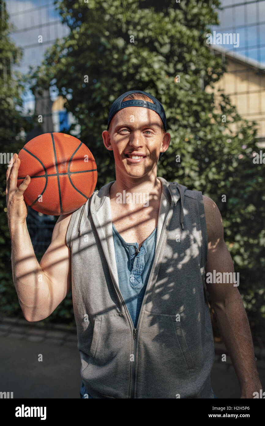 Ritratto di bel giovane giocatore di basket tenendo una palla. Teenage streetball player sul tribunale aperto guardando la fotocamera. Foto Stock