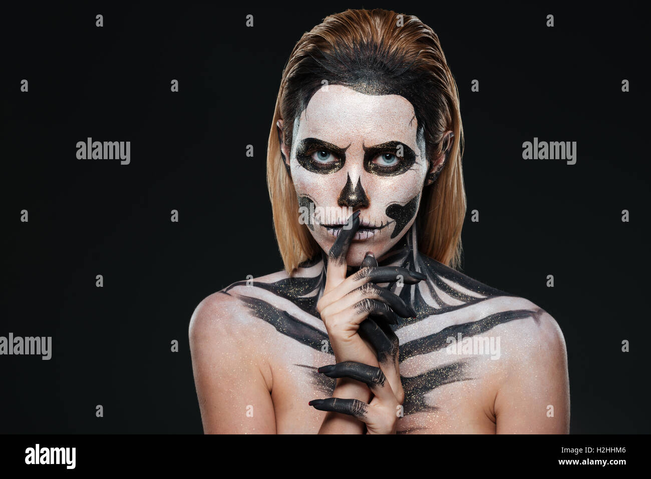 Donna con paura Halloween trucco che mostra il silenzio gesto su sfondo nero Foto Stock