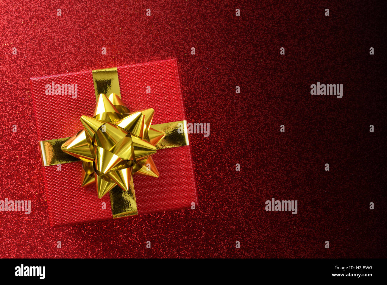 Confezione regalo rossa con fiocco e decorazioni in oro su rosso brillante tabella strutturata e degradata a nero. Vista superiore Foto Stock