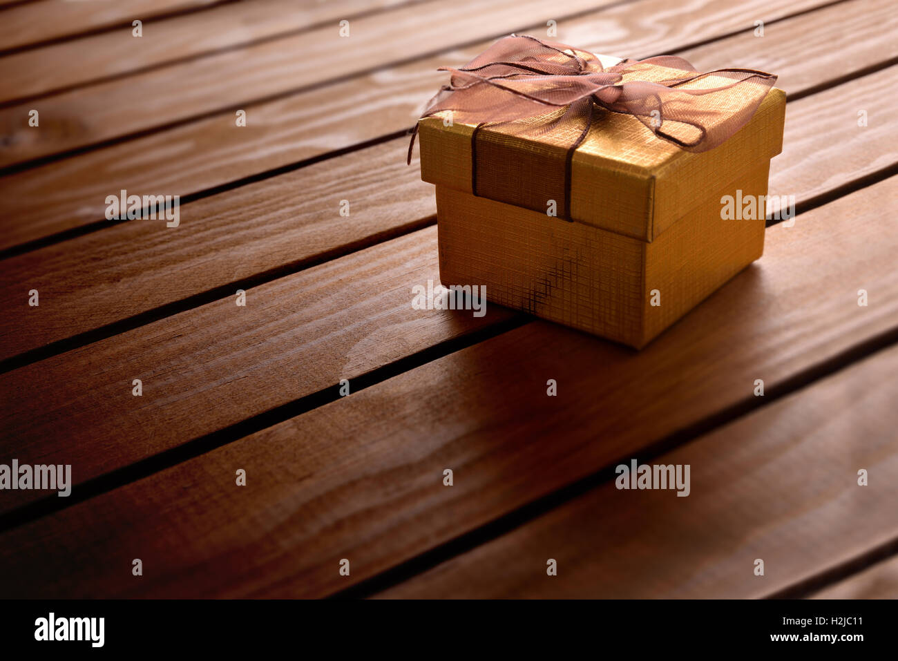 Golden confezione regalo con nastro marrone sul tavolo diagonale assicelle di legno. Vista in elevazione Foto Stock