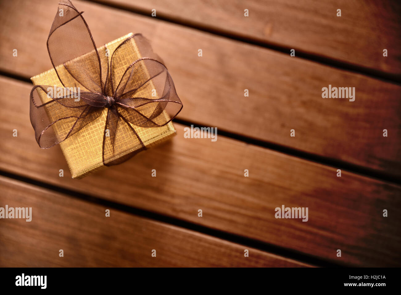 Golden confezione regalo con nastro marrone sul tavolo diagonale assicelle di legno. Vista superiore Foto Stock
