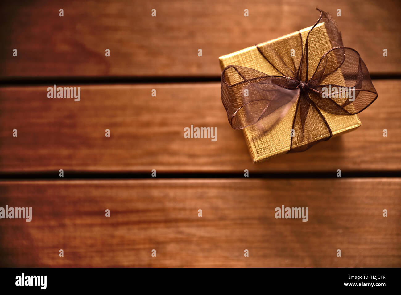 Golden confezione regalo con nastro marrone sul tavolo assicelle di legno. Vista superiore Foto Stock