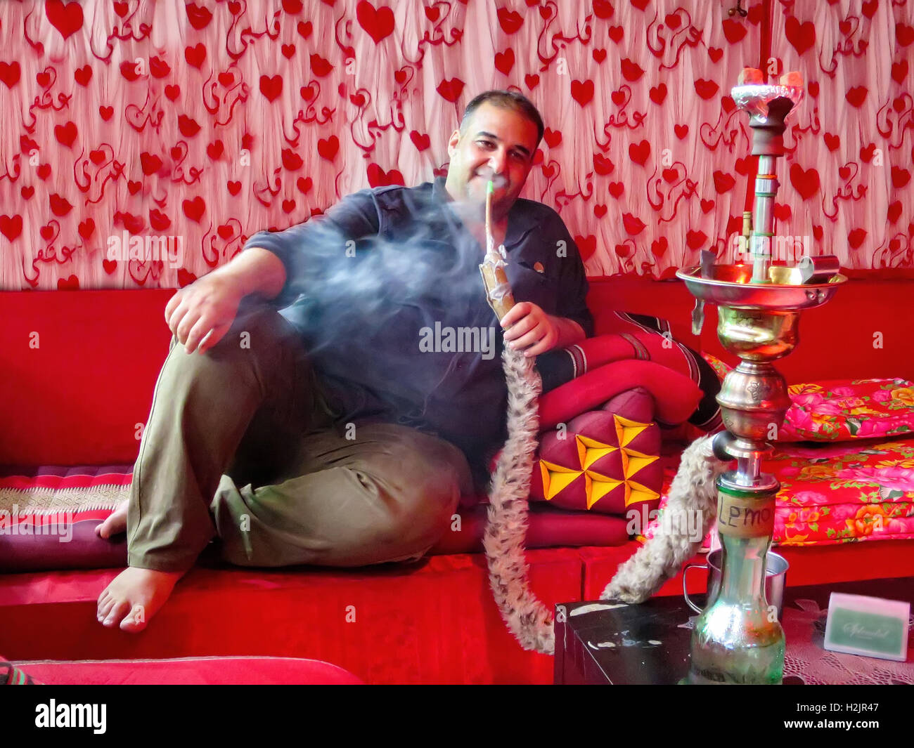 Un iracheno uomo si siede su un divano rosso è fumare shisha, tubo di acqua, in un caffè di Kuala Lumpur, Malesia. Foto Stock