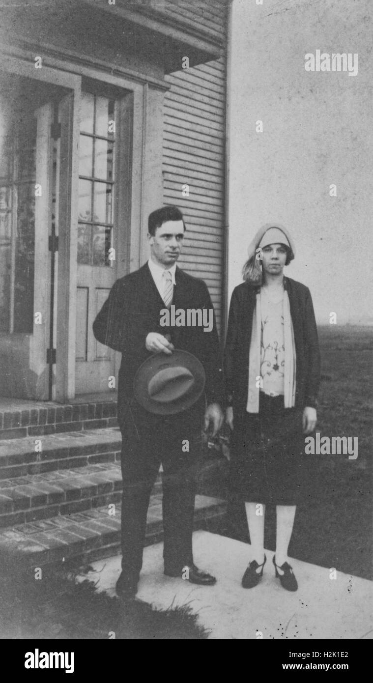 Unknown City, Stati Uniti - Gennaio 01, 1950: una giovane coppia stand sui loro passi davanti alla loro casa, l'uomo con un cappello nero alla sua vita, la donna che guarda avanti e che appare cupa, 1950 Foto Stock