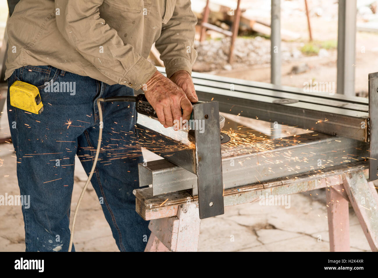 Builder fabbricazione di monconi in acciaio per la casa di ristrutturazione utilizzando una smerigliatrice per tagliare e acciaio liscio Foto Stock