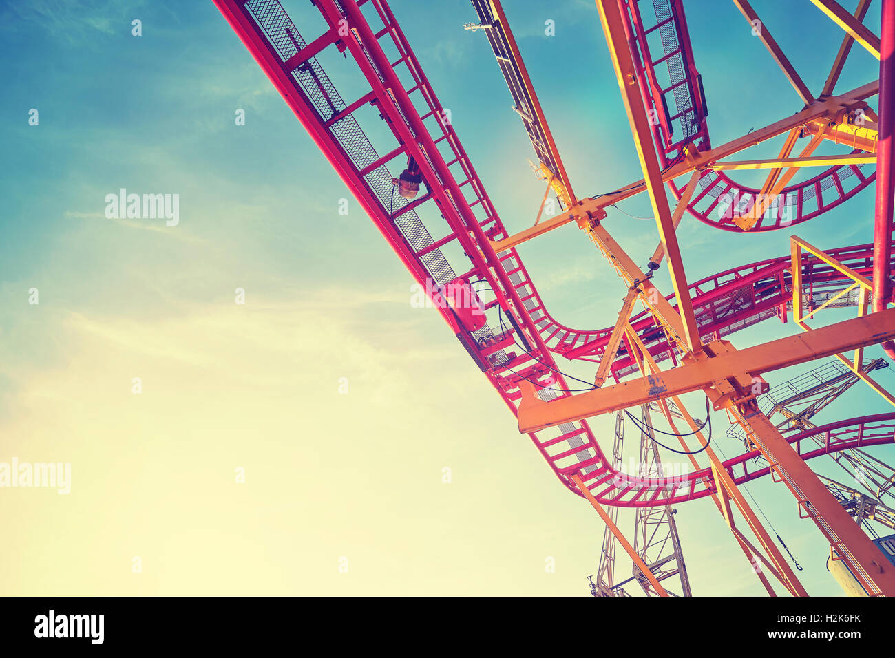 Vintage filtrata roller coaster via la costruzione di un parco di divertimenti al tramonto, spazio per il testo. Foto Stock