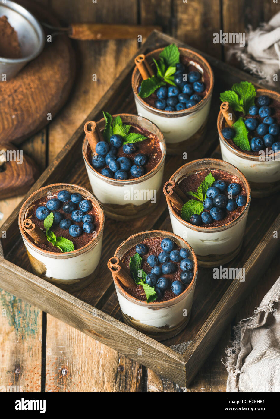 In casa il Tiramisù dessert in bicchieri con cannella, menta e ai mirtilli freschi nel vassoio in legno su legno rustico sfondo, top v Foto Stock