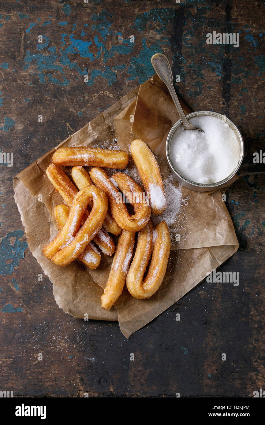 Tradizionale spagnola trattare churros con zucchero semolato, servita sulla carta da forno con la scatoletta di latta di zucchero la targhetta ovale su woode scuro Foto Stock