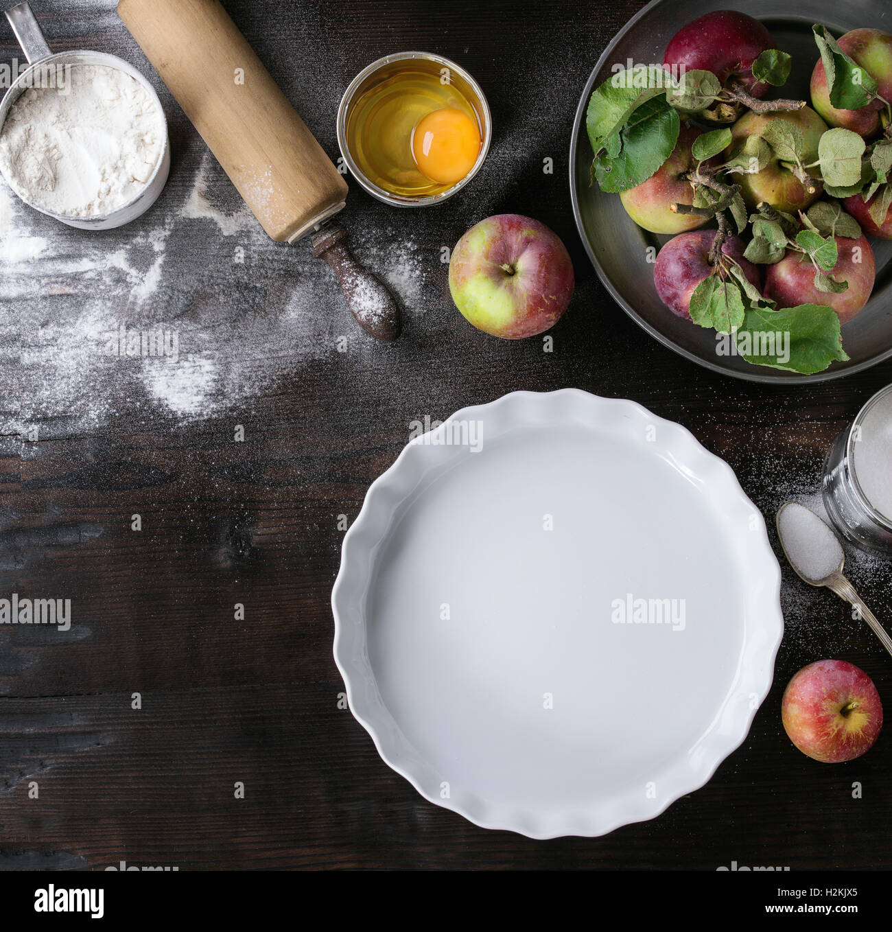 Ingredienti per la produzione di torta di mele. Farina, zucchero, uova rotte in lattine di lattina, mele fresche con foglie in una piastra di metallo, cottura bianco f Foto Stock