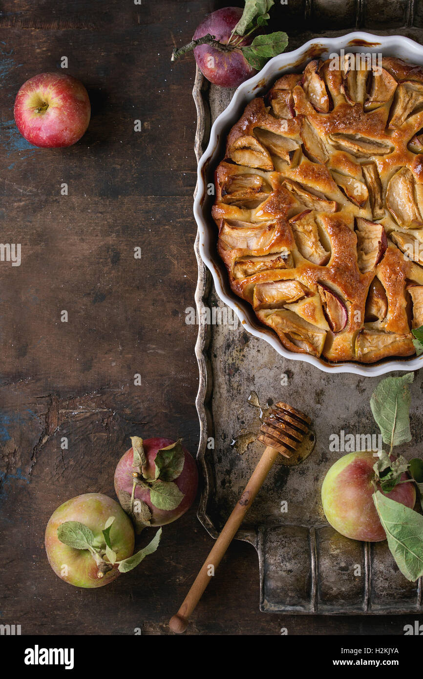 In casa torta di mele torta in bianco forma ceramica su metallo vintage vassoio con mele fresche con foglie e miele su legno scuro bac Foto Stock