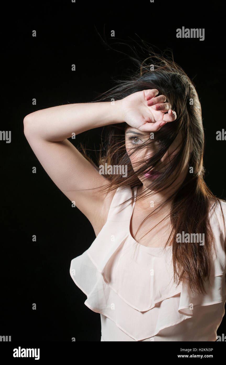 Donna in piedi nel vento capelli che copre il viso e le mani sopra la testa Foto Stock