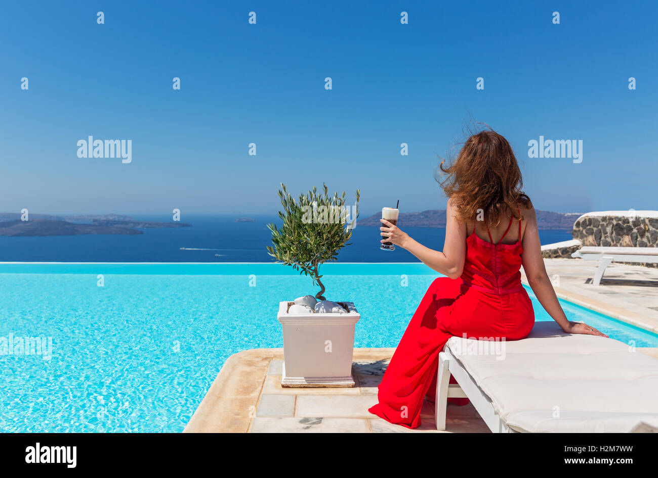 La donna in abito rosso con un drink sullo sfondo della piscina Foto Stock