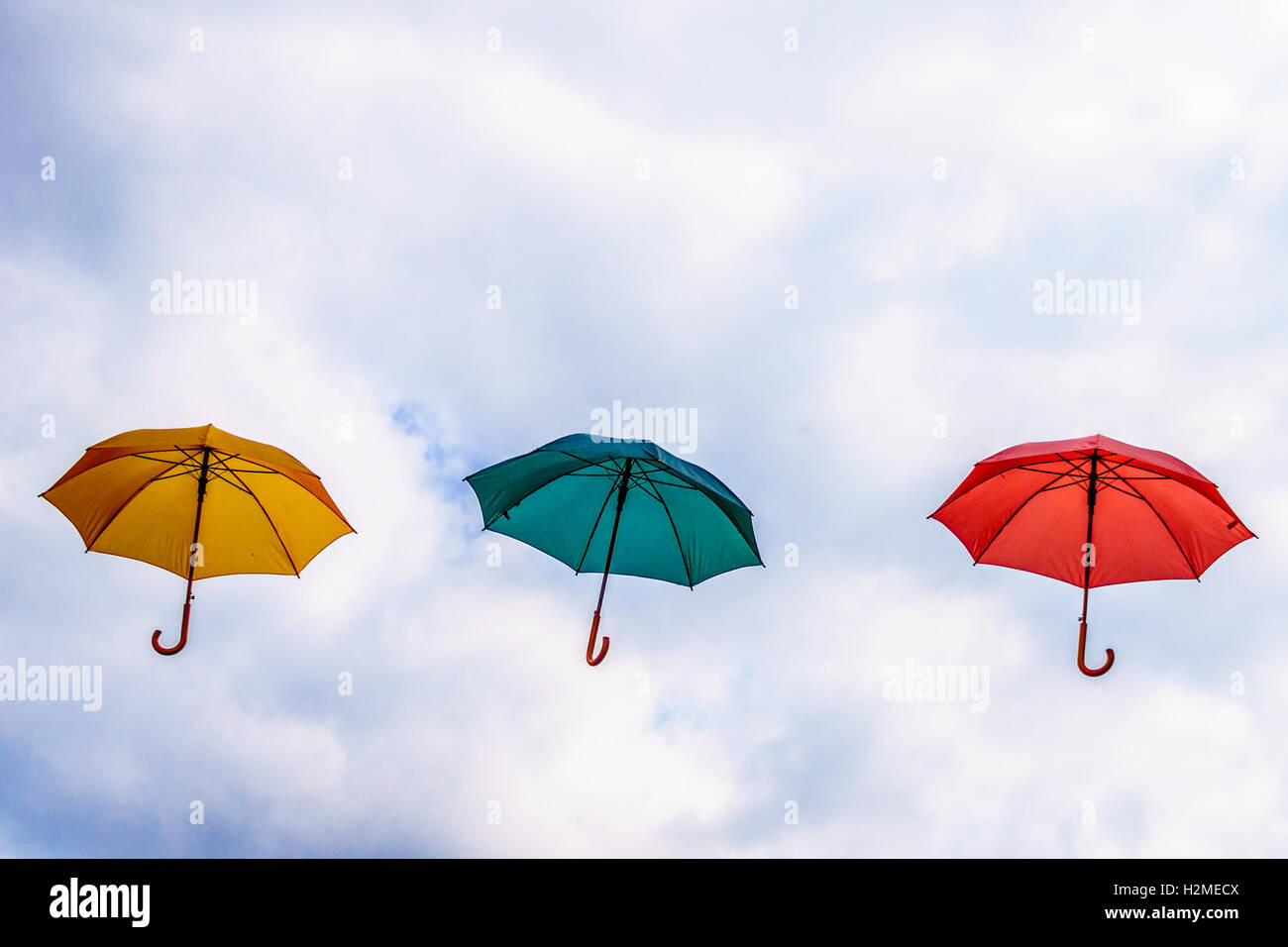 Ombrello giallo e verde Ombrellone rosso ombrello galleggianti in aria sotto parzialmente il cielo blu con nuvole periodi. Foto Stock